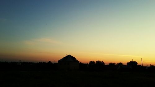 Silhouette house on field against orange sky