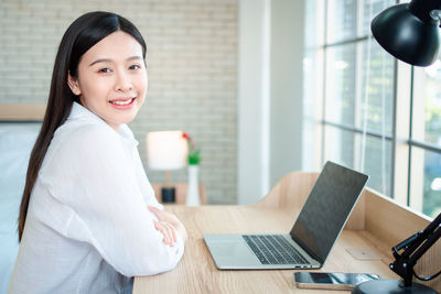 Portrait of smiling young woman using laptop on table