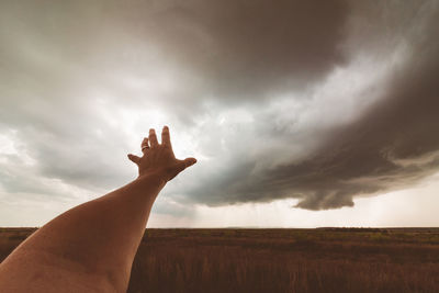 Cropped hand of person against cloudy sky