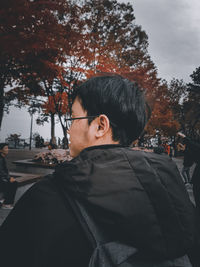 Portrait of young man looking away against trees