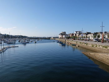 Sailboats in harbor by buildings against clear blue sky