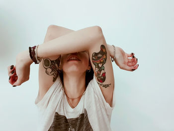 Young woman with tattoos covering face with hands over white background