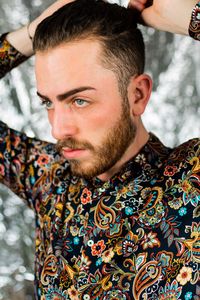 Young man looking away tying hair standing against defocused background