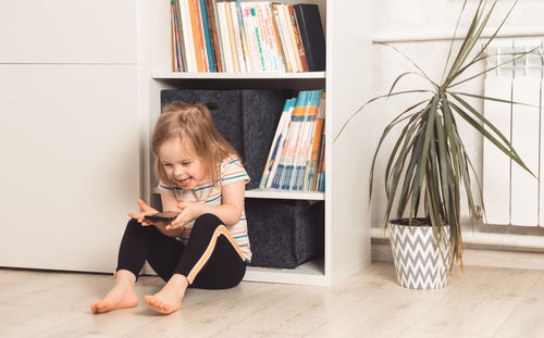 Little child sits on the floor in his room and uses the phone. smiling girl looking at the phone. 