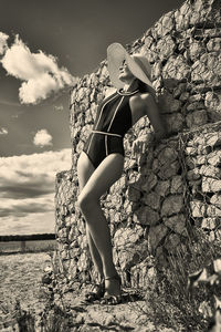 Portrait of a woman in a swimsuit, hat and sunglasses in summer on the riverbank by a concrete wall