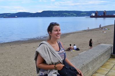 Young woman smiling while sitting on railing at beach