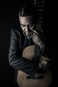 Man hugging guitar against black background