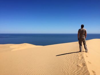 Rear view of man standing on sand dune against clear sky