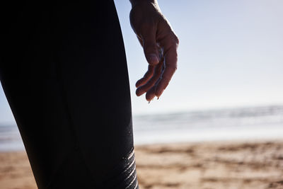 Midsection of person standing at beach against sky