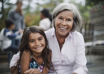 Portrait of happy grandmother sitting with granddaughter at yard