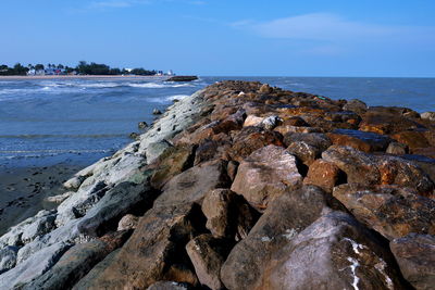 Rocks on shore by sea against sky
