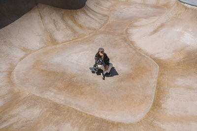 Young woman sitting on skateboard at sports ramp