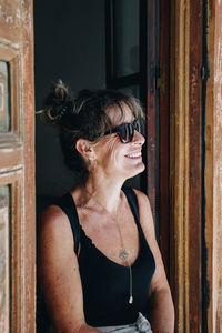 Portrait of young woman wearing sunglasses while standing against wall