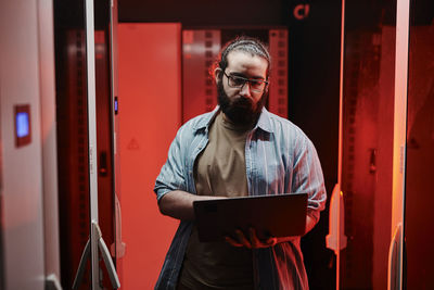 It expert working on laptop in server room with red neon light