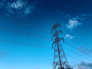 Low angle view of electricity pylon against blue sky