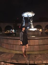 Full length of woman standing against illuminated building at night