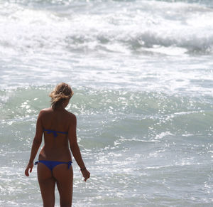 Rear view of woman wearing bikini standing in sea during sunny day