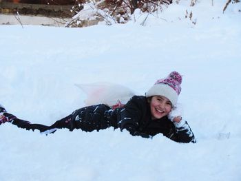 Portrait of happy girl lying down on snow covered field