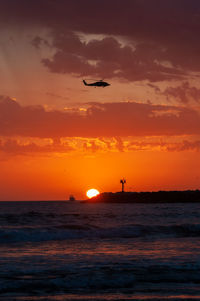 Silhouette airplane flying over sea against sky during sunset