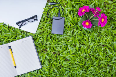 High angle view of open book with mobile phone charger and flowers on grassy field