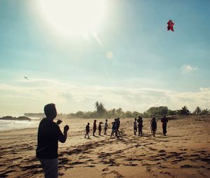 Man flying kite at beach against bright sky