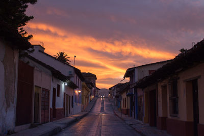 Street amidst city against sky at sunset