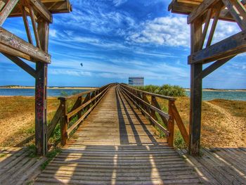 Empty boardwalk leading towards sea against sky