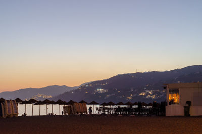 Illuminated buildings and mountains against clear sky at sunset