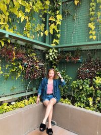 Full length of beautiful woman sitting by plants