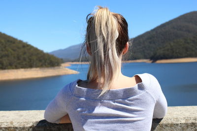 Rear view of woman standing at lake against sky