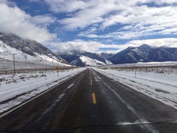 Road leading towards snowcapped mountains against sky