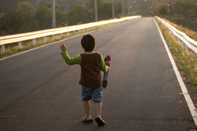 Rear view of boy holding tripod while walking on road