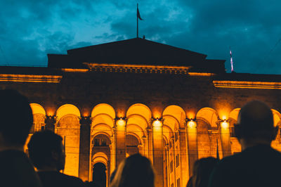 People walking in illuminated city against sky