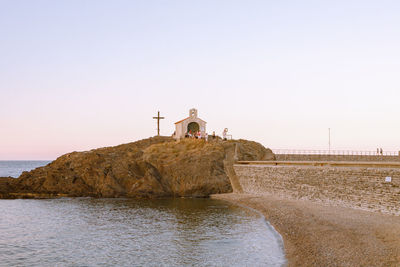 People on lighthouse by sea against clear sky