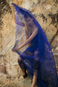 Full length woman wearing blue net fabric while standing against rock formation