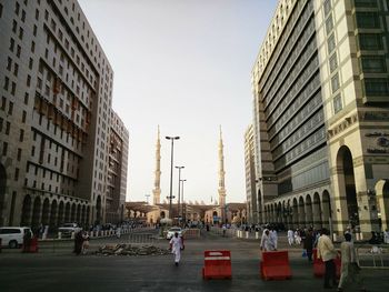 People on street amidst buildings in city against clear sky