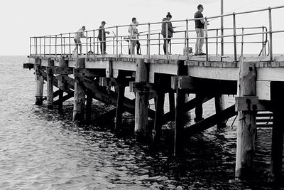 People standing on pier while fishing in sea