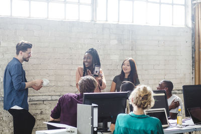 Cheerful businesswoman showing mobile phone to team while looking at male colleague in office