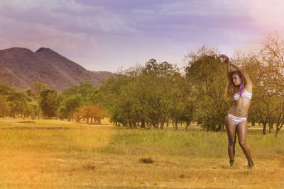 Full length of young woman standing on field against sky