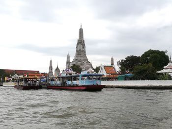 Boats in river by buildings against sky