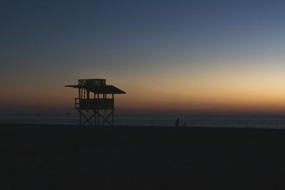 Silhouette lifeguard hut on beach against sky during sunset
