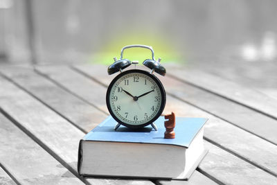 Close-up of alarm clock and chess piece on book at table