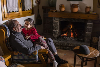 High angle view of girl with grandfather sitting on armchair at home