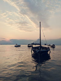 Sailboats moored on sea against sky during sunset