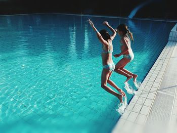 Full length of siblings in bikini jumping into swimming pool