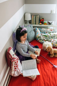 High angle view of girl in fairy costume reading book while sitting on bed at home