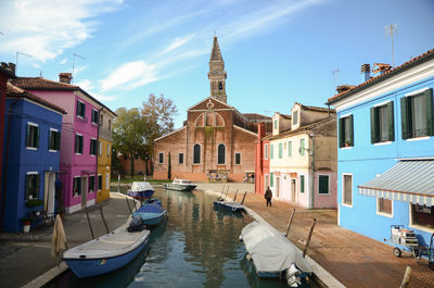 Boats moored in canal by buildings against sky in city