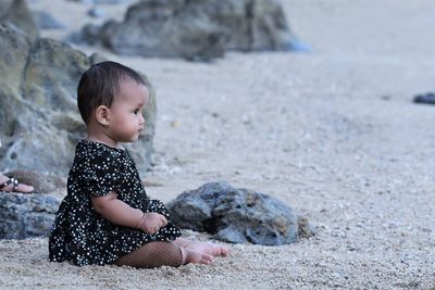 Side view of little girl sitting on rock
