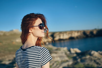 Portrait of young woman wearing sunglasses standing against sky