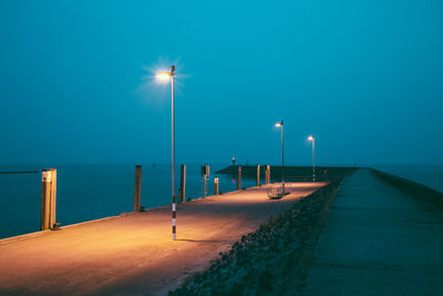 Illuminated street light on beach against clear blue sky at night